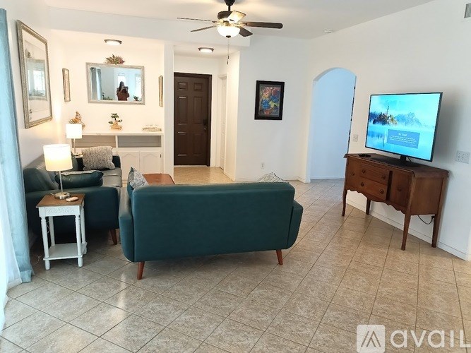 A living room with a green couch, a television, and a ceiling fan.