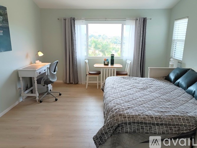 A bedroom with a large bed, a desk with a chair, and a window with curtains.