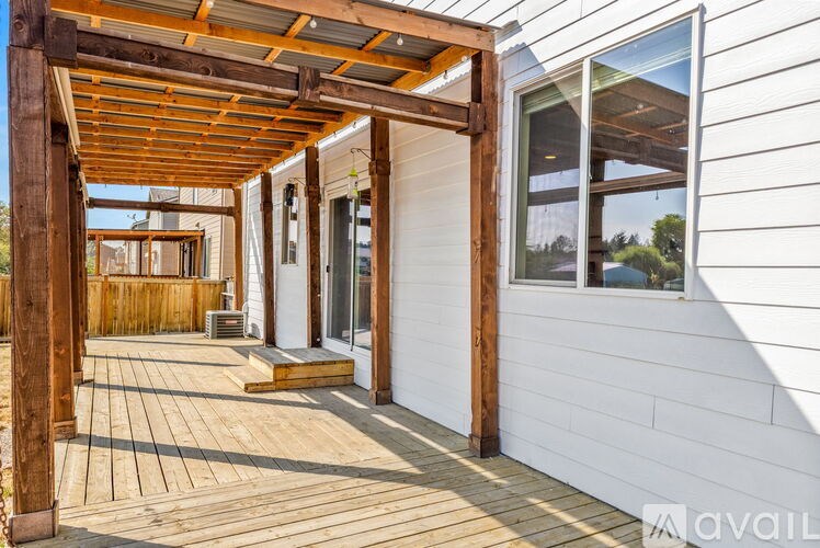 A wooden deck with a pergola and a white house with a window.