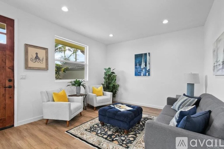 A living room with a grey couch, two white chairs, a blue ottoman, and a rug.