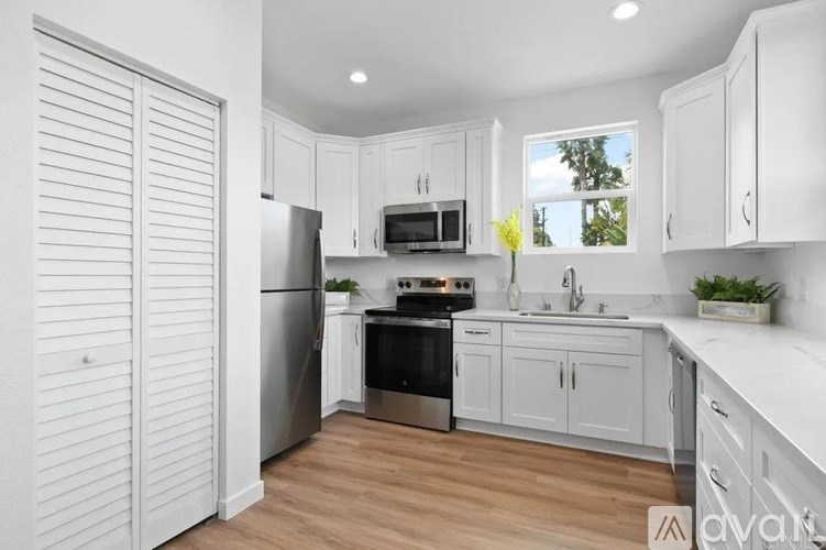 A kitchen with white cabinets and appliances, a window with a view of trees outside, and a wooden floor.