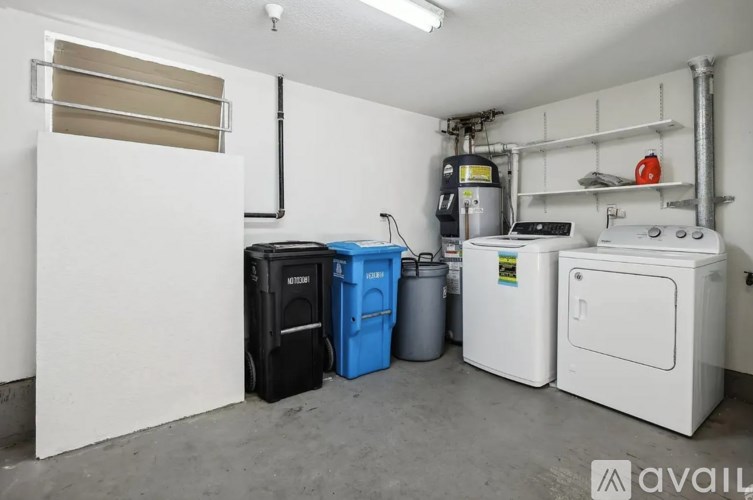 A room with a white fridge, a black bin, a blue bin, and a white washing machine.