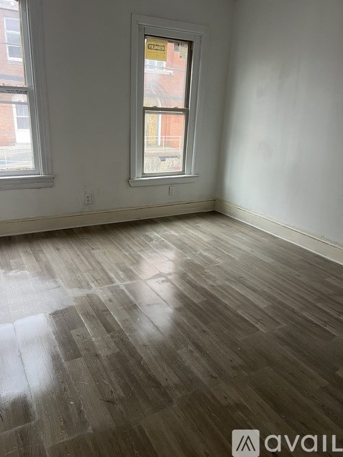 A room with wooden flooring and a window showing a red brick building outside.