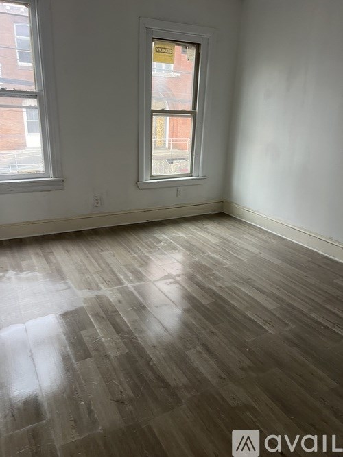 A room with wooden flooring and a window showing a red brick building outside.