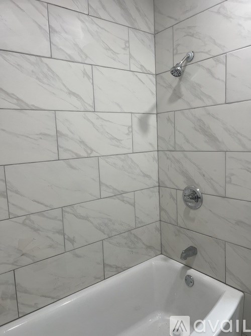 A white bathroom with a white tub and a white shower head.