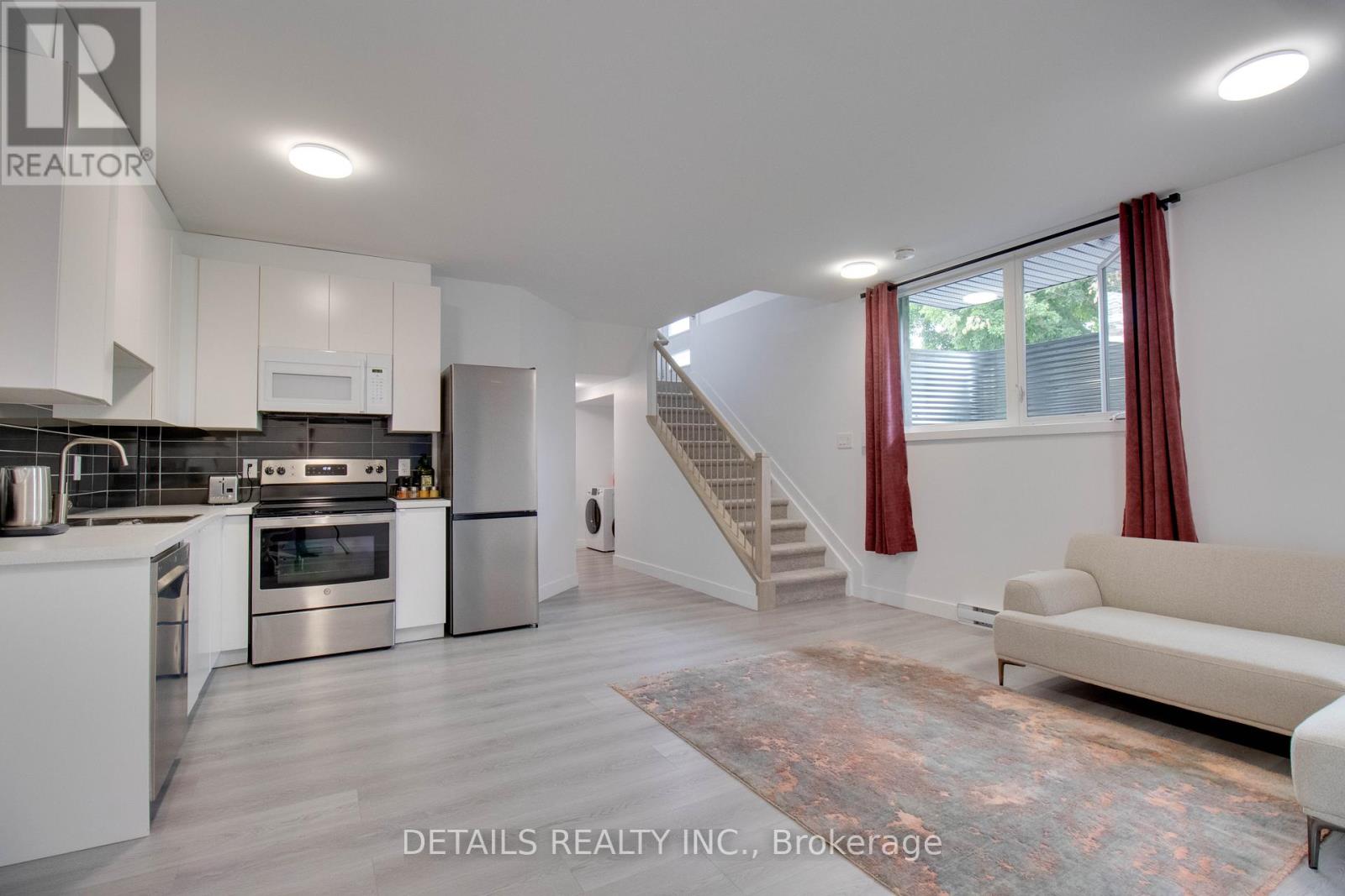 A modern kitchen with stainless steel appliances and a staircase in the background.