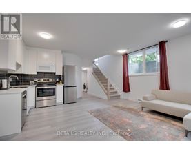 A modern kitchen with stainless steel appliances and a staircase in the background.