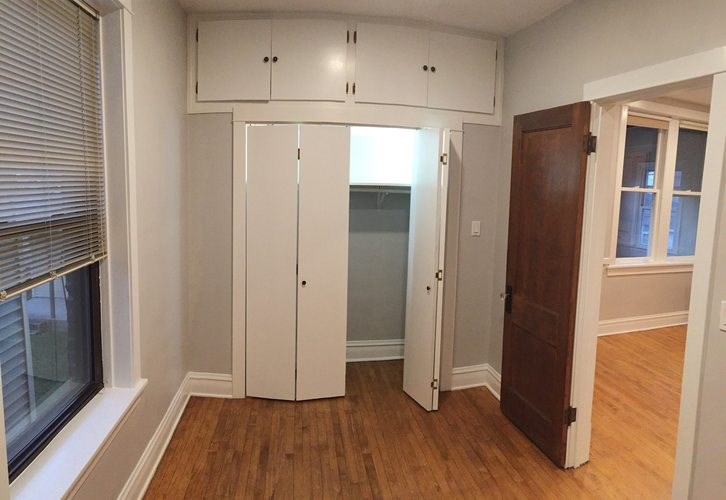 A room with a wooden floor and a white wall with a window and a door.