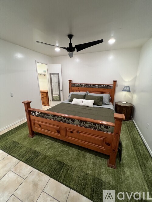 A bedroom with a bed, green carpet, and a ceiling fan.