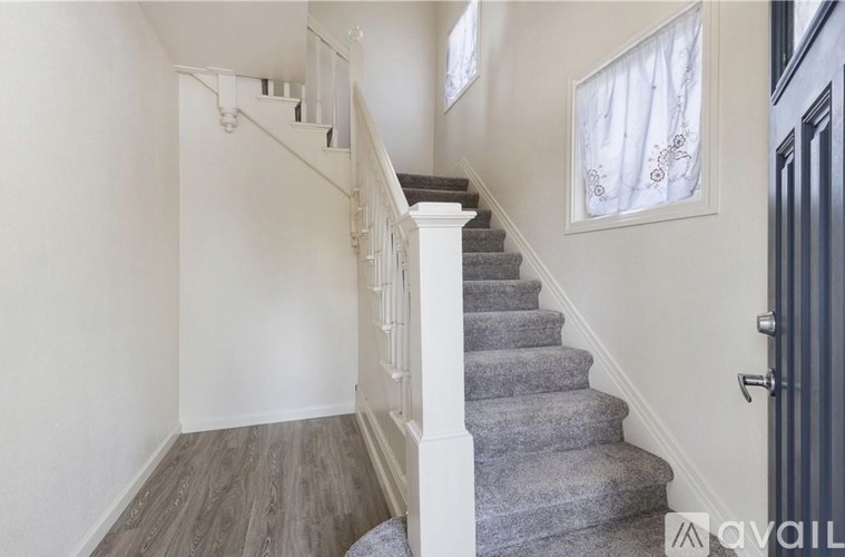 A staircase with a grey carpeted runner and white balusters leads up to a white door.