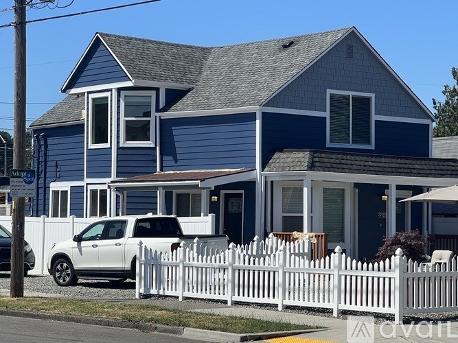 A blue house with a white picket fence and a white car parked in front.
