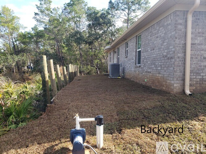 A backyard with a brick house, a mailbox, and a pipe.