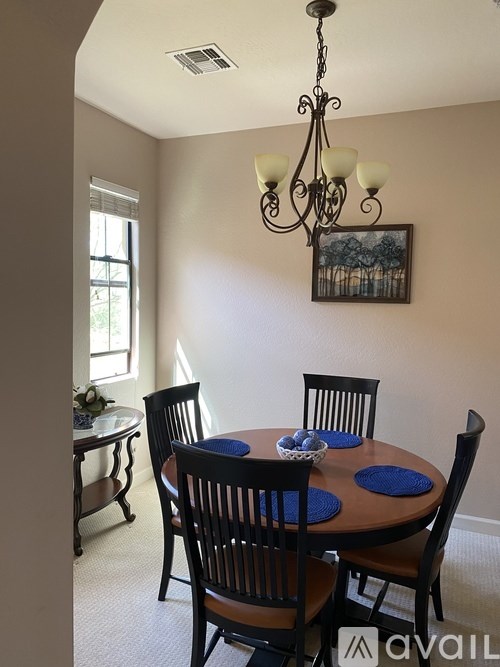 A dining room with a chandelier, a table with blue placemats, and chairs.
