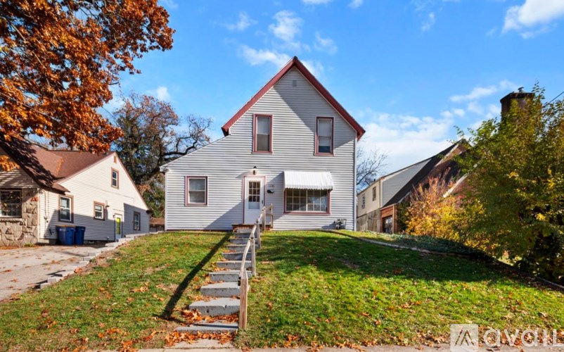 A house with a white exterior and a red roof is surrounded by a grassy lawn and trees with autumn leaves.