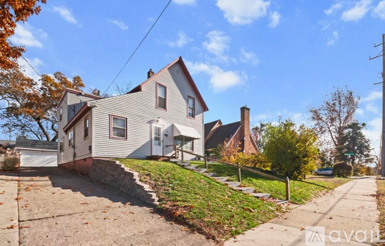 A house with a grey siding and a white door is surrounded by a grassy area and a sidewalk.