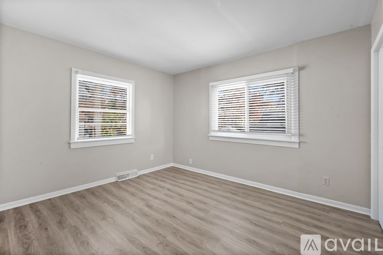 A room with wooden flooring and two windows with blinds.