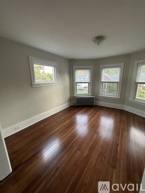 A room with wooden flooring and three windows.