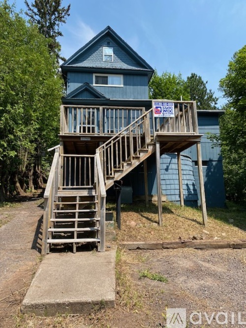 A house with a blue exterior and a wooden deck with stairs leading up to it.