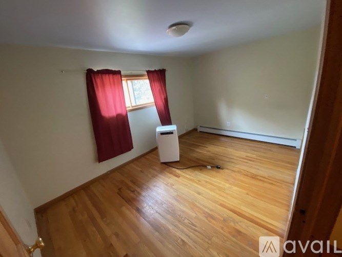 A room with wooden floors and a window with red curtains.