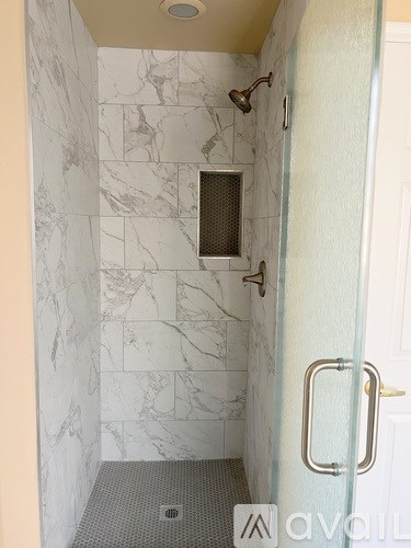 A bathroom with a marble tile shower and a glass door.