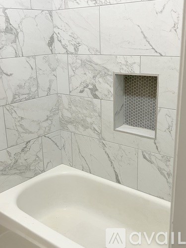 A white bathtub in a bathroom with marble tiles.