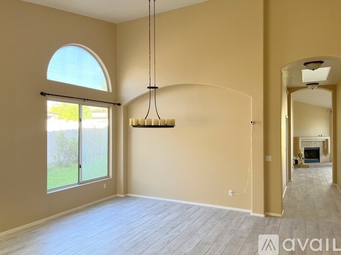 A large, empty room with a large arched window and a chandelier hanging from the ceiling.