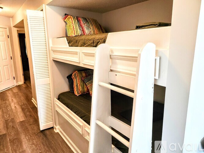 A white bunk bed with a green mattress and a striped pillow is in a room with wooden flooring.