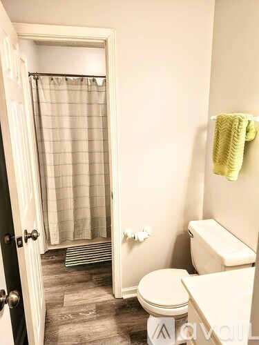 A bathroom with a toilet, a shower curtain, and a towel hanging on the wall.