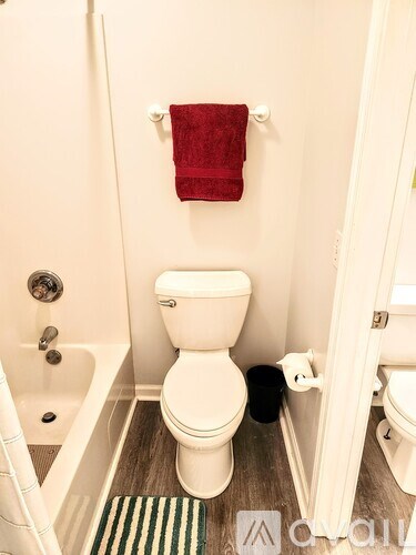 A white toilet with a red towel hanging on the wall.