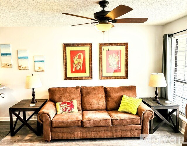 A brown couch with a green pillow is in the middle of a room with a ceiling fan.