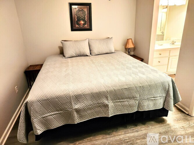 A bed with a grey comforter and two pillows sits in a room with a lamp and a mirror.