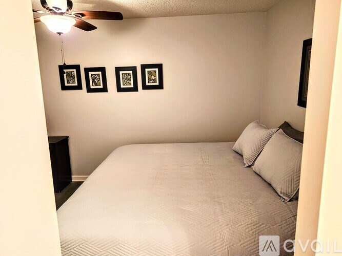 A bedroom with a bed, pillows, a ceiling fan, and picture frames on the wall.