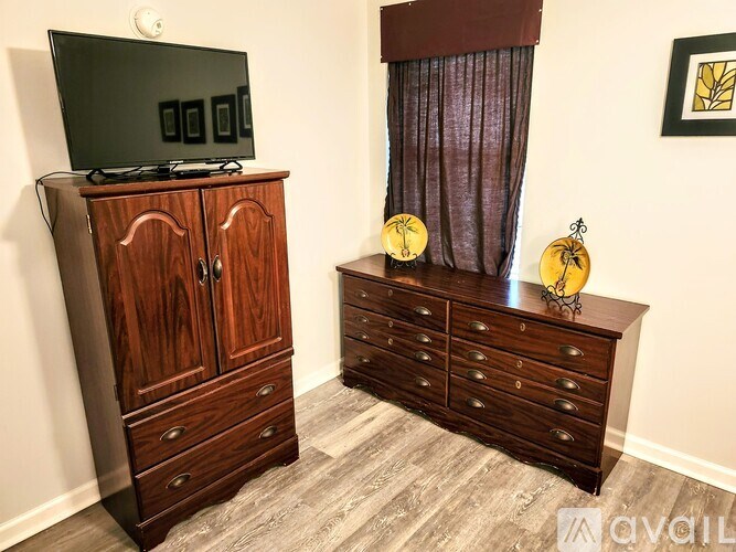 A wooden cabinet with a television on top and a dresser with a curtain beside it.