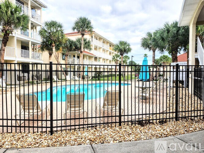 A black fence surrounds a pool area with chairs and palm trees.