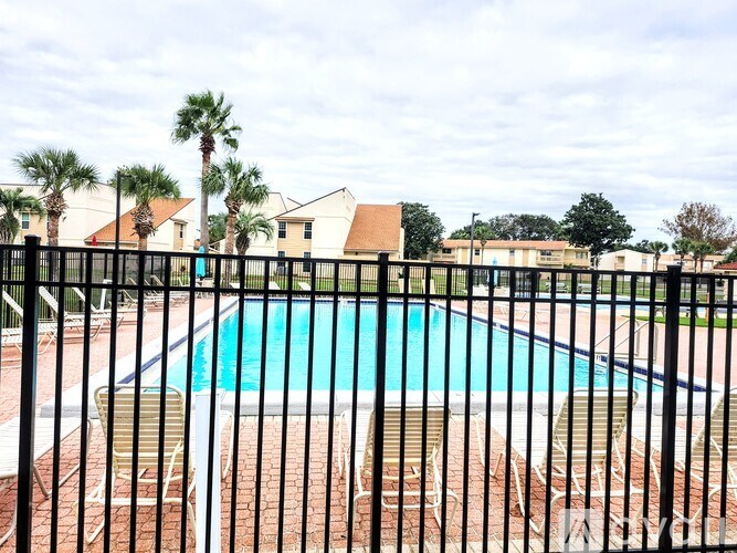 A pool surrounded by a black fence with chairs around it.