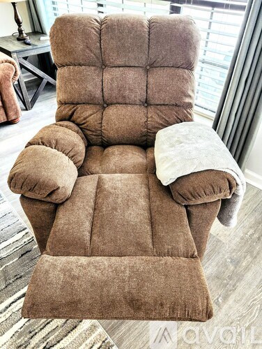 A brown recliner chair with a pillow and a blanket on it.