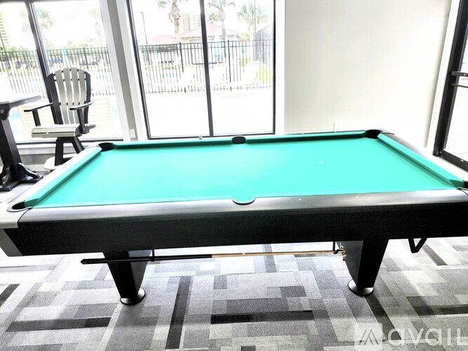 A pool table in a room with a chair and a view of a fence and trees outside.