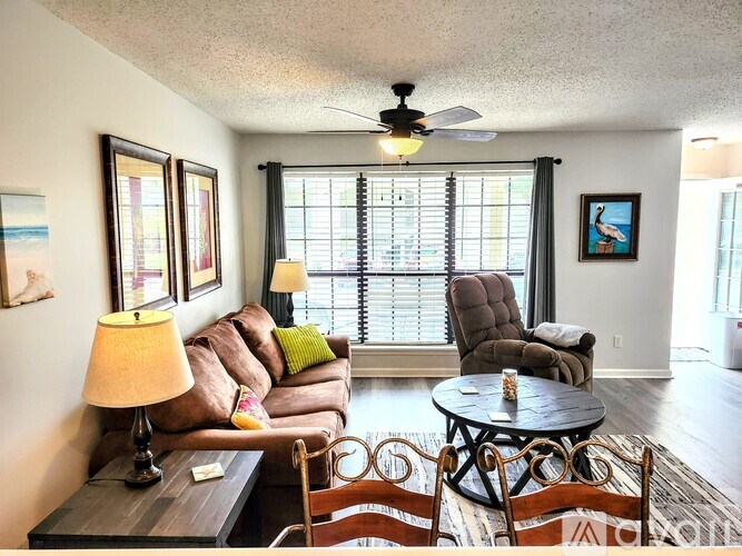 A living room with a brown couch, a chair, a table, and a ceiling fan.