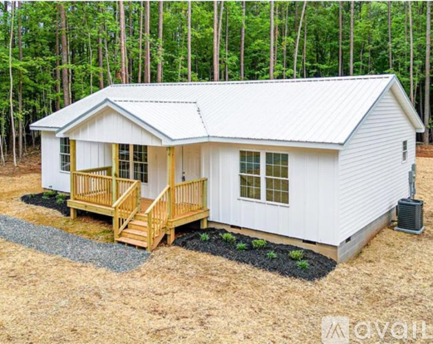 A small white house with a porch and a metal roof is surrounded by trees.