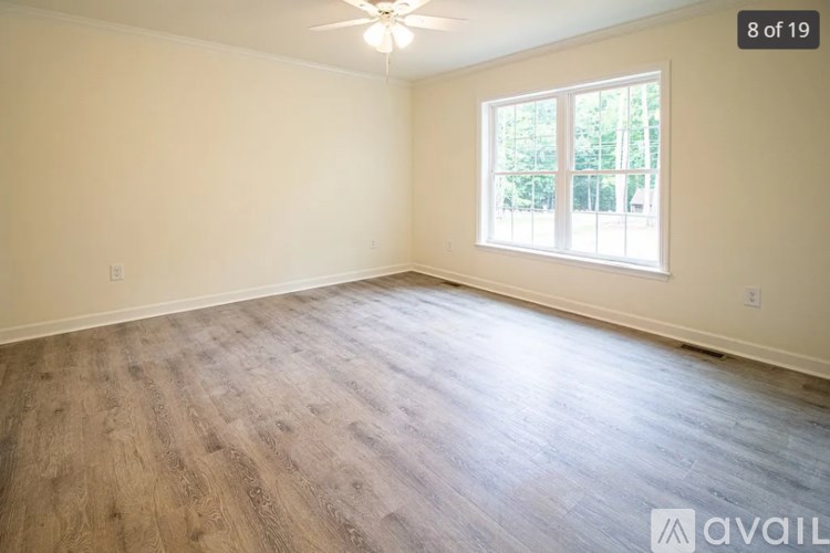 A room with wooden flooring and a window with a view of trees.