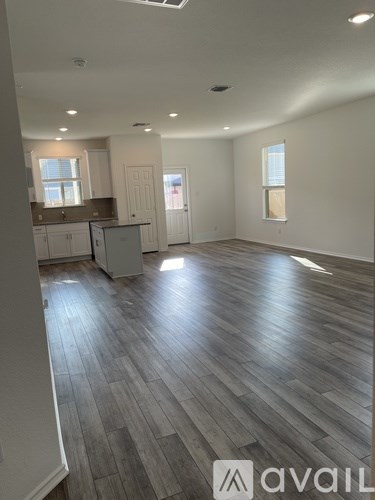 A spacious room with wooden flooring and a kitchen area in the background.