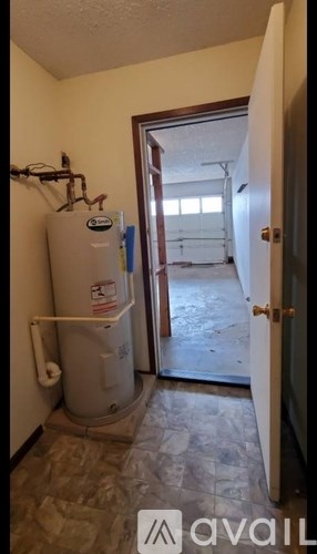 A room with a water heater and a door leading to another room.