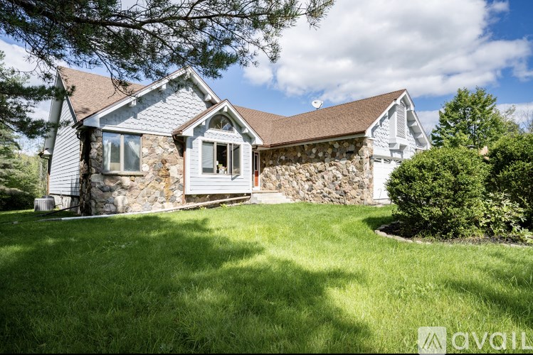 A house with a stone wall and a brown roof is surrounded by a green lawn.