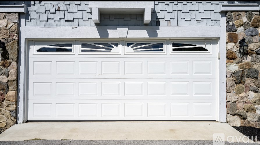 A white garage door is closed and has a stone wall on the left side.