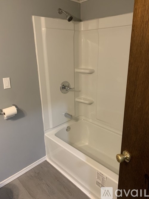 A white bathtub with a shower head and a toilet paper roll on the wall.