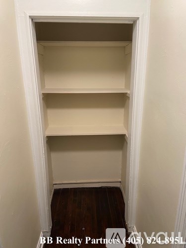 A white shelving unit with four shelves is in a corner of a room with white walls.
