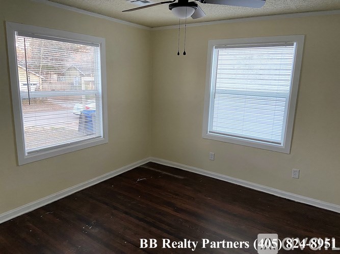 A room with a ceiling fan and two windows.