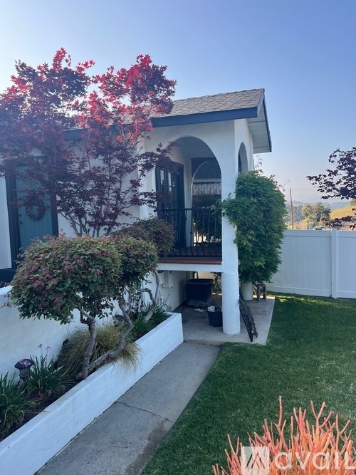A white house with a red tree in front.