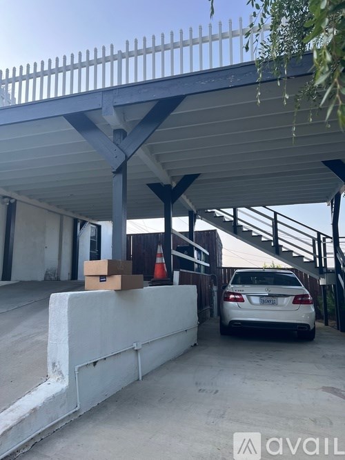 A car is parked under a covered area with a box on the ground.