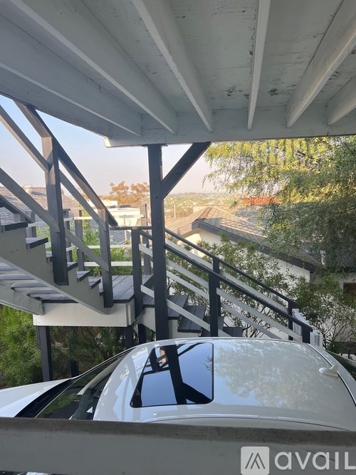 A car is parked under a covered area with a staircase leading to a building.